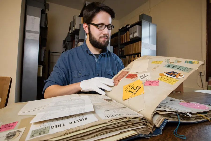 Information sciences graduate student Joseph Porto searches through the scrapbook of a student who attended the university 100 years ago. 