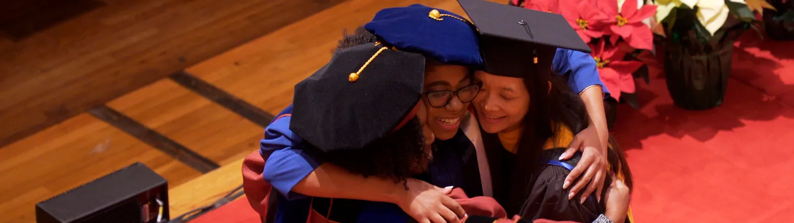 A graduate hugging two faculty hooders