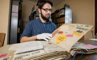 Information sciences graduate student Joseph Porto searches through the scrapbook of a student who attended the university 100 years ago. 