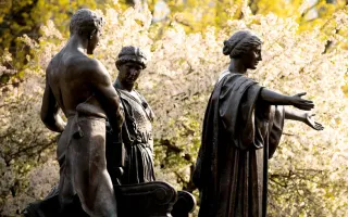 Statue of Alma Mater with Learning, and Labor in front of yellow and white spring blooming trees.