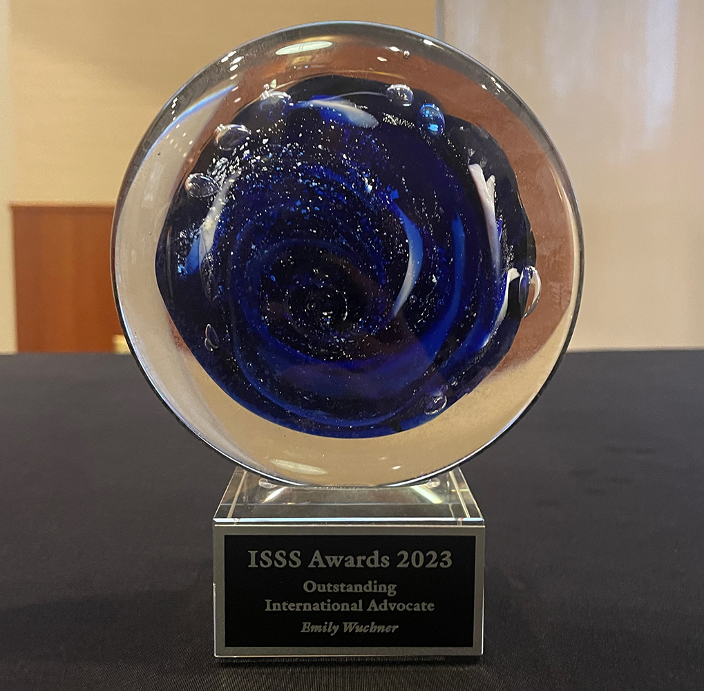 Wuchner's award sits on a table. It reads: ISSS Awards 2023, Outstanding International Advocate, Emily Wuchner